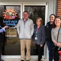 Group photo of volunteers in front of Kids' Food Basket entrance.